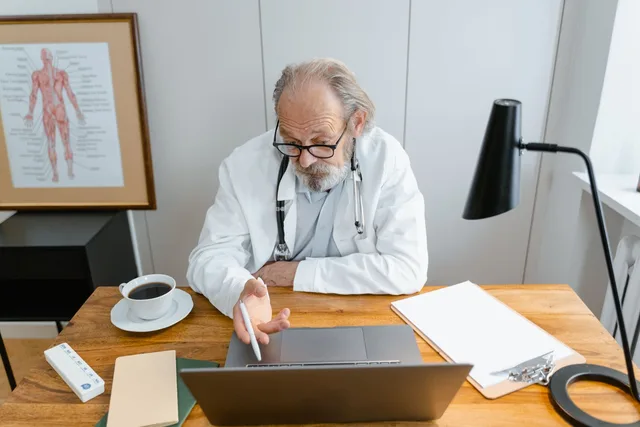 Arzt am Schreibtisch seiner Praxis mit Laptop und Unterlagen