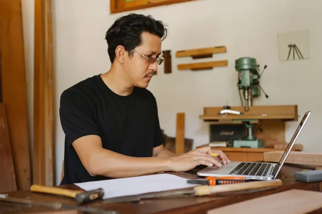 Handwerker an der Werkbank mit Laptop und Unterlagen